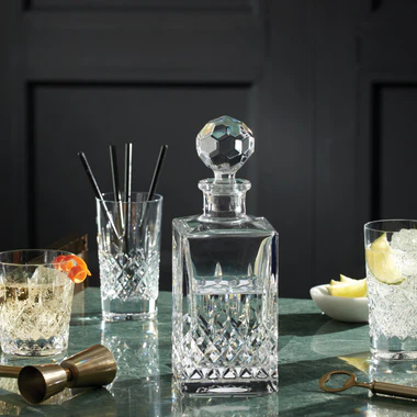 Crystal decanter with cocktail glasses and bar tools on a dark surface